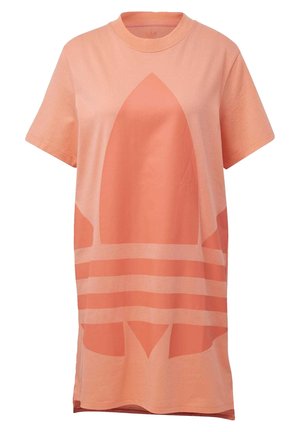 Personne à la peau foncée portant une robe T-shirt ample de couleur pêche avec un grand logo et des baskets blanches avec des accents pêche.