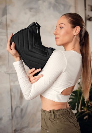 Černá prošívaná taška s chevron vzorem, se stříbrným zipem a kovovými akcenty, kterou drží modelka v zkráceném bílém topu.