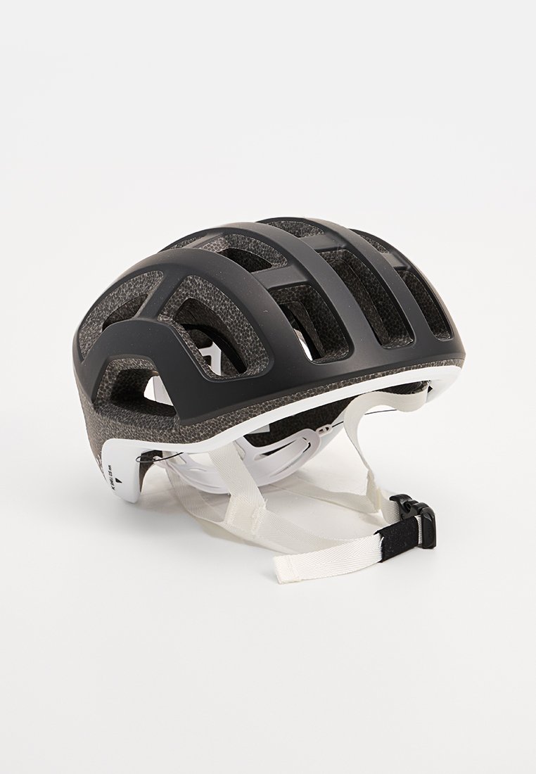 Casco da ciclismo nero con texture opaca, ampie fessure di ventilazione, fibbie regolabili bianche e un design aerodinamico elegante.