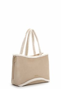 Borsa tote beige con bordo bianco peloso e due manici. Materiale morbido simile alla pelle scamosciata, forma strutturata e dettaglio del logo dorato sul davanti.