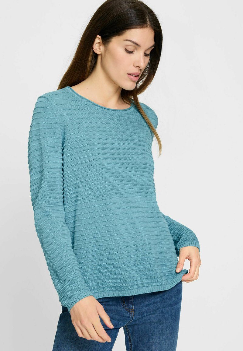 Türkiser Pullover mit langen Ärmeln, der über strukturierte horizontale Streifen, einen runden Halsausschnitt und gerippte Bündchen verfügt, getragen mit Jeans.