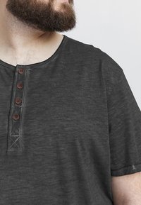 Tricou scurt cu mânecă, de culoare gri închis, realizat dintr-un material moale, cu guler rotund și patru nasturi mici maro pe băga.
