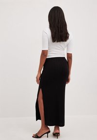 Falda maxi negra acanalada con una apertura alta en el lateral, combinada con una camiseta blanca ajustada y sandalias negras de tacón. Textura suave, diseño ceñido.
