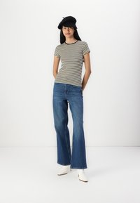 Strikket svart og hvit t-skjorte, blå vide jeans og hvite ankelstøvler; svart beret fremhever det uformelle antrekket.