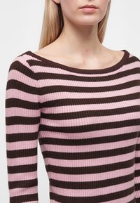 Femme portant un pull côtelé à rayures horizontales rose et marron foncé avec une encolure large et arrondie.
