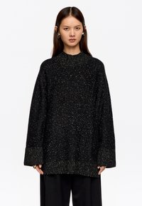 Sudadera negra de gran tamaño con un patrón texturizado y moteado, y puños acanalados; presenta un cuello alto y un corte relajado.