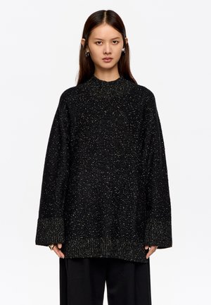 Czarny, oversize sweter z teksturowanym, nakrapianym wzorem oraz ściągaczami u rękawów; ma wysoki dekolt i luźny krój.