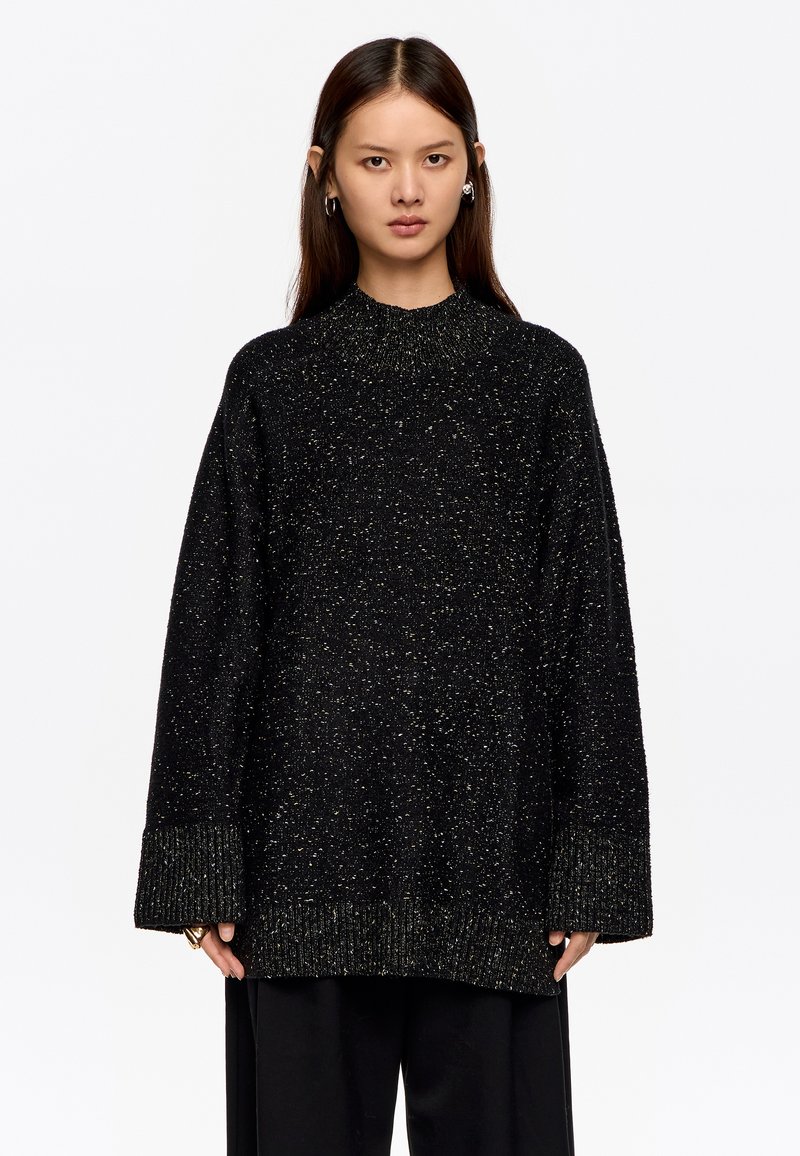 Sudadera negra de gran tamaño con un patrón texturizado y moteado, y puños acanalados; presenta un cuello alto y un corte relajado.