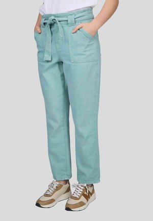Pantalons en coton turquoise clair avec une taille nouée, des poches latérales et une coupe fuselée. Portés avec des baskets beiges et brunes.