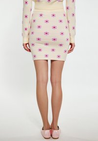 Häkelt Minirock in Creme mit rosa und lila Blumenmustern. Figurbetontes Design, weicher Stoff und betonter Taillenbund. Kombiniert mit rosa Schuhen.