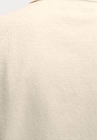 Nahaufnahme eines crèmefarbenen Stoffes, der eine glatte Textur und sichtbare Nähdetails entlang der Naht zeigt.