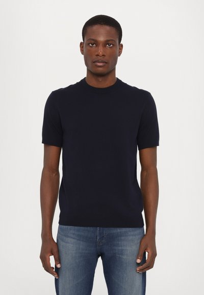 Navy short-sleeve crewneck knit sweater made of soft material, featuring a fitted design and smooth texture, paired with light blue denim jeans.