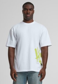 White cotton t-shirt with oversized fit, featuring a bright yellow abstract design on the left side and a classic crew neckline.