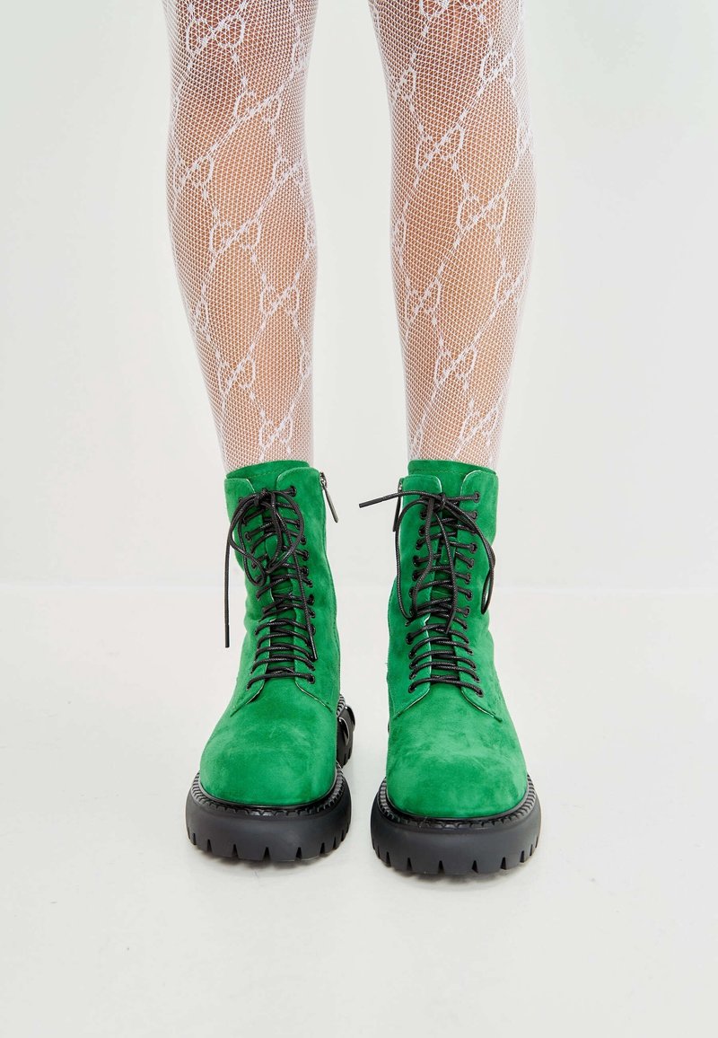 Botas de tobillo verde de ante con cordones, suelas de goma negra gruesa y detalles texturizados, combinadas con medias de red blancas con un patrón de lazo.