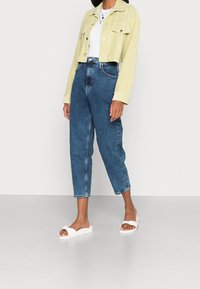 Lichtgroen corduroy cropped jasje, wit T-shirt, hooggetailleerde blauwe jeans en witte instapsandalen. De jeans hebben een rechte pasvorm en minimale details.