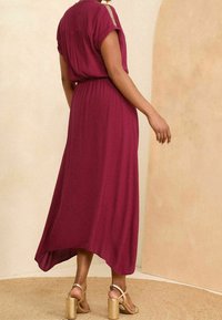 Pitkä burgundinvärinen mekko, jossa on rento malli, käännetyt hihat ja elastinen vyötärö. Yhdistetty kultaisiin korotettuihin sandaaleihin. Sujuva kangas, virtaava muotoilu.