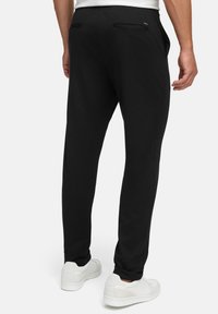 Sorte joggebukser laget av mykt stoff, med en avsmalnende design, elastisk midje og baklommer. Sammen med hvite sneakers.