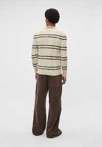 Kaķa krāsas džemperis ar melnām svītrām, raksturīga pinuma tekstūra, ribota aproces un apakšmala. Kombinēts ar vaļīgām brūnām kordurojas biksēm.