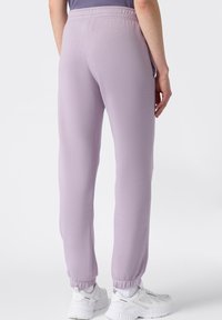 Pantalones de chándal lilas con un diseño ajustado, cinturilla elástica y puños elásticos en los tobillos. Tejido texturizado, combinados con zapatillas blancas.