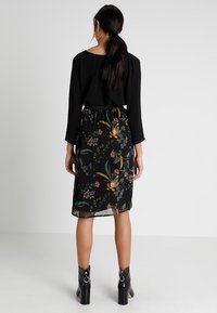 Haut à manches longues noir associé à une jupe noire à motifs floraux. La jupe présente des fleurs vives, une taille élastique et une couche transparente. Bottes à talons noires.