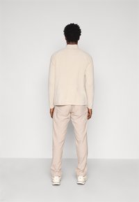 Hele beež kudumisseelik tekstuuriga viimistlusega, kombineeritud helebeežide pükstega. Valged tossud täiendavad rõivastust, vaadates tagant.