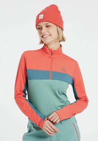 Dugi rukav sportski majica u koraljnoj i tirkiznoj boji s četvrtastim patent zatvaračem, visokim ovratnikom i prozračni materijal. Sadrži logo i dizajn s kontrastnim panelima.
