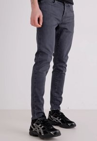 Ciemnoszare jeans o slim fit z delikatnym przetarciem, z pięcioma kieszeniami i szlufkami na pasek, połączone z czarnymi butami sportowymi.