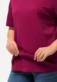 Fuchsia kortærmet t-shirt lavet af bomuld, med rund halsudskæring, afslappet pasform og synlig søm detaljer, holdt nederst.