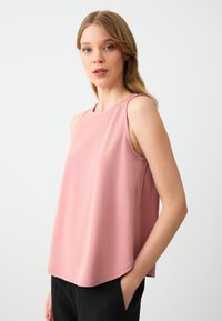 Top senza maniche rosa con una vestibilità rilassata, scollo rotondo e texture liscia. Abbinato a pantaloni neri, che mettono in mostra uno stile informale.