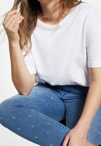 Camiseta blanca de manga corta con un escote redondo, combinada con unos vaqueros azules claros que presentan un sutil patrón para añadir textura.