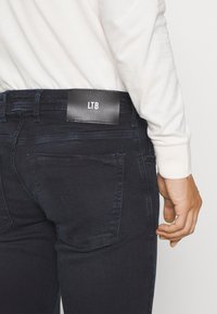 Jeans de denim azul oscuro con una textura suave, que cuentan con un diseño de bolsillo trasero y una etiqueta negra con "LTB" cerca de la cintura.