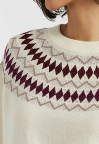 Maglione lavorato a maglia color crema con un motivo geometrico in bordeaux e beige attorno allo scollo. Il materiale sembra morbido e testurizzato.