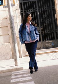 Traper jakna s dvostrukim kopčanjem preko svijetloružičaste košulje, uparena s mornarskoplavim hlačama širokih nogavica. Urbano okruženje s pješačkim prijelazom.