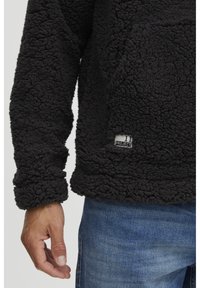 Sort fleece-pullover med en tekstureret, fluffy overflade. Har et sidemærke med "11 PROJECT" og en design med afslappet pasform.