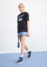 Svart T-shirt med flerfärgad grafik och detalj i rhinestone, ihop med en denimkjol och marinblå sneakers. Innehåller vita sportstrumpor.