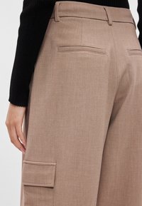 Μπεζ παντελόνι φαρδιάς γραμμής με λεία υφή, διαθέτει πίσω τσέπες και ραφές, συνδυασμένο με μαύρο ριγωτό τοπ.