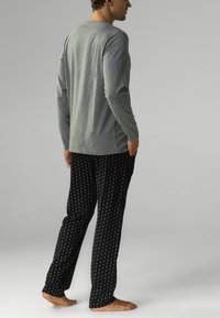 Szary longsleeve z okrągłym dekoltem w połączeniu z czarnymi spodniami piżamowymi w wzory z białymi kropkami, wykonanymi z miękkiego materiału, o luźnym kroju.