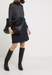 Svart vävd tote-väska med en texturerad yta, kombinerad med en mörkgrå långärmad topp och en figursydd svart kjol. Långa svarta läderstövlar.