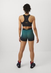 Soutien-gorge de sport noir avec un design dos nageur, doté d'une bande texturée. Short dégradé teal assorti, ajusté avec une taille noire et un logo. Bottes noires avec des accents rouges.