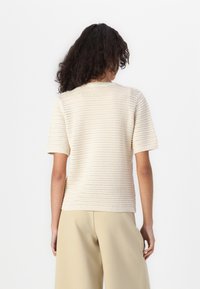 Gebreide crèmekleurige trui met korte mouwen, voorzien van een gestructureerd ontwerp en ronde halslijn. Draag met beige wijde broek, achterkant zichtbaar.