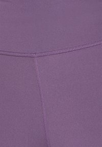 Fialové legíny s hladkým, strukturovaným povrchem, s přiléhavým střihem a kontrastním stehem podél švů pro zvýraznění detailu.