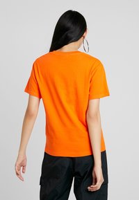 Camiseta de algodón naranja de manga corta con cuello redondo. Textura suave, corte relajado y sin patrones ni gráficos visibles en la parte trasera.