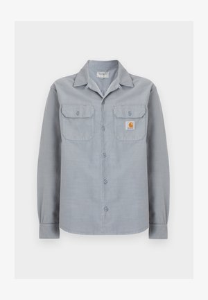 Jasnoszara koszula na długi rękaw zapinana na guziki, z dwoma kieszeniami na piersi, z których jedna po prawej stronie ma małą naszywkę z logo Carhartt.