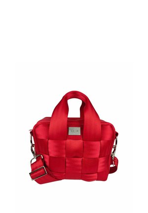 Pieni punainen kudottu kangaslaukku, jossa lyhyet kahvat, säädettävä olkahihna ja hopeanväriset metalliosat valkoisella taustalla.