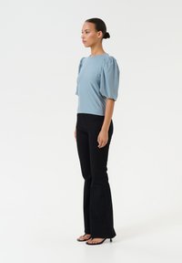 Light blue short-sleeve blouse with puffed sleeves, paired with black flared pants and black heeled sandals, against a white background.