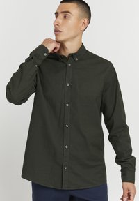 Camisa de botones de color verde oscuro con cuello, mangas largas y cierre de botones en la parte frontal. Fabricada con una tela suave y de textura lisa.