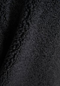 Tela de forro polar negro con una superficie suave y texturizada, que presenta un patrón de bucles que añade profundidad y calidez.