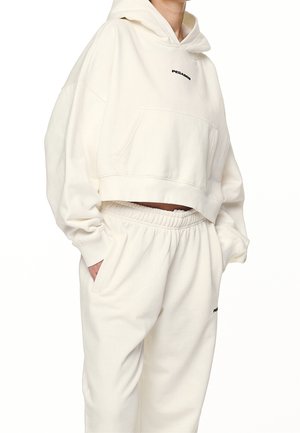Person wearing off-white cropped hoodie with front pocket and matching sweatpants with elastic waist and side pockets.