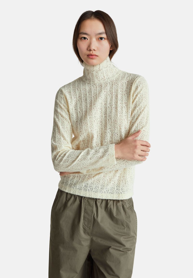 Maglione a collo alto di colore crema con motivo floreale, maniche lunghe e design aderente, abbinato a pantaloni larghi verde oliva.
