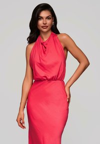 Robe à encolure halter en corail lumineux, présentant un corsage drapé et une jupe cintrée. Le tissu a une finition douce et texturée avec un léger éclat.
